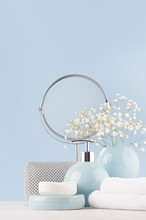 Dressing Table With Circle Mirror, Cosmetic Silver Accessories And White Small Flowers In Ceramic Pastel Blue Vase On White Wood Board, Closeup, Vertical.
