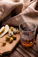 Wall Mural - Rustic still life with whiskey and snacks. Crystal glass with a beautiful pattern on a wooden table. Snack for whiskey on crumpled paper olives, crackers, cheese, almonds, pear, apple.