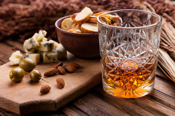 Wall Mural - Rustic still life with whiskey and snacks. Crystal glass with a beautiful pattern on a wooden table. Snack for whiskey on crumpled paper olives, crackers, cheese, almonds, pear, apple.