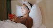 © leungchopan - Woman apply face mask on bed and use of the cellphone at night