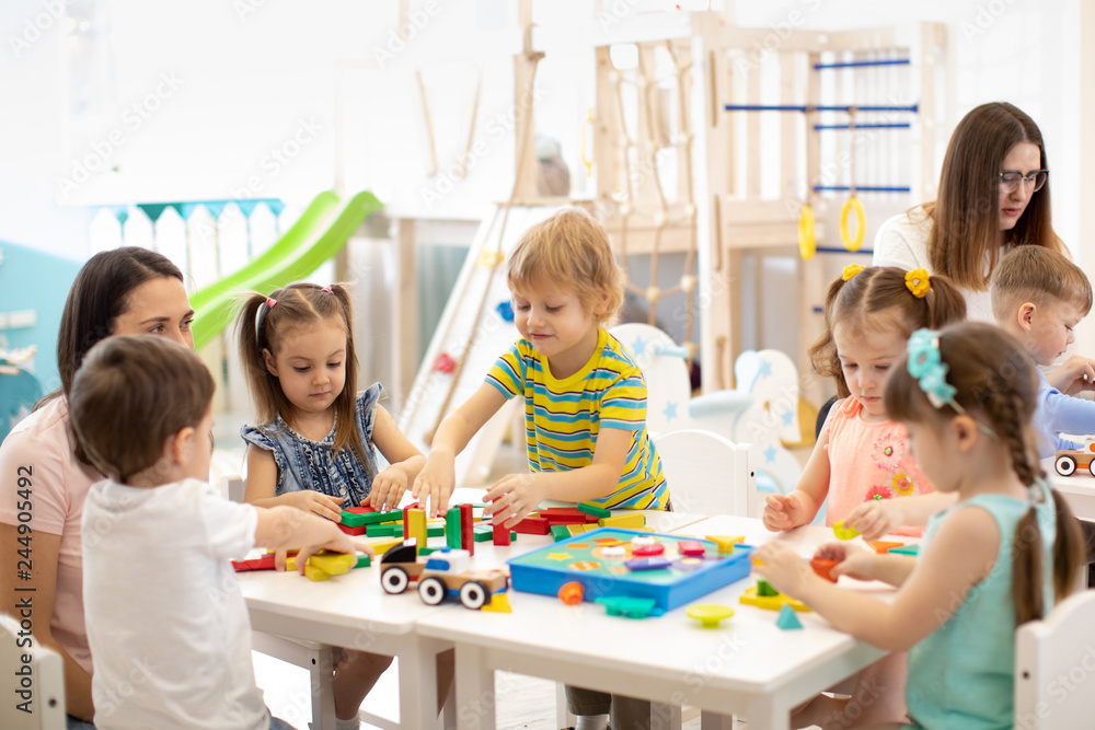 Kindergarten children playing toys with teacher in playroom at preschool. Education concept. - obrazy, fototapety, plakaty 