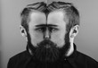 © Leika production - Black and white photo of a man with a beard and stylish hairdo dressed in the black shirt standing next to the mirror with reflection of part of his face