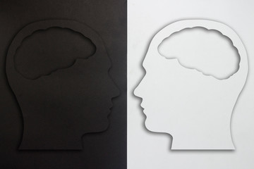 Two paper heads with a brain silhouette, black and white on a black and white background. The concept of a split personality, different opinions, dispute, war. Flat lay, top view.