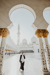 Wall Mural - Traditionally dressed arabic woman standing on sun shine wearing black burka visiting Sheikh Zayed Grand Mosque in Abu Dhabi, United Arab Emirates.