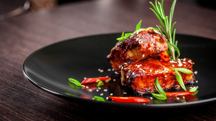 The concept of American cuisine. Roasted pork ribs, baked and glazed in barbecue sauce. Serving dishes in the restaurant on a black plate with sesame and micro green. Next to a glass of red wine.