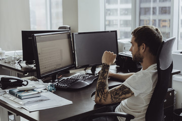 Stylish business man with tattoos working on the computer in the office