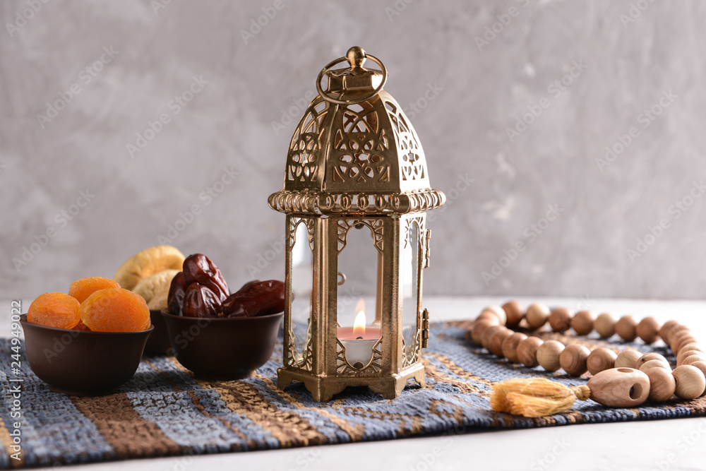 Muslim lantern with prayer beads and dried fruits on table
