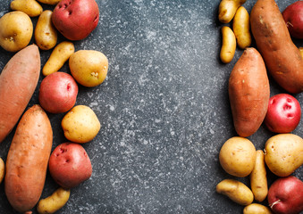 Variety of raw uncooked organic potatoes: red, white, sweet  and fingers potatoes over dark texture background.