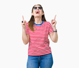 Middle age mature woman wearing sunglasses over isolated background amazed and surprised looking up and pointing with fingers and raised arms.