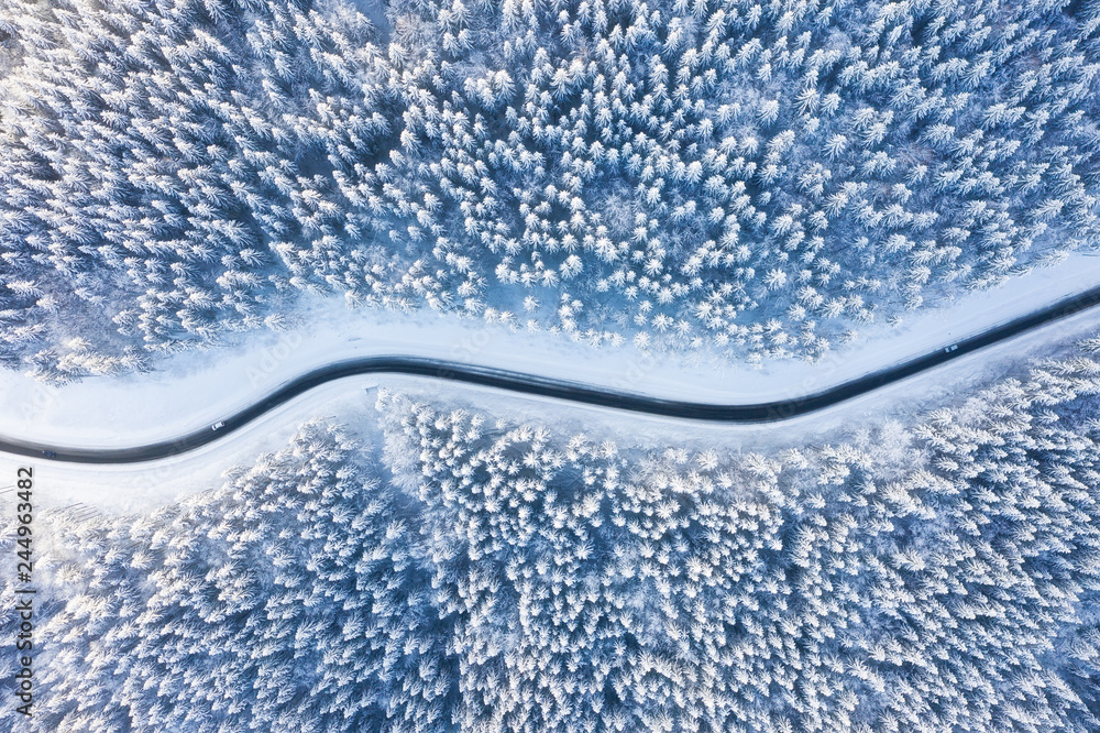 Aerial view on the road and forest at the winter time. Natural winter landscape from air. Forest under snow a the winter time. Landscape from drone - obrazy, fototapety, plakaty 
