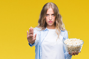 Wall Mural - Beautiful young blonde woman eating popcorn over isolated background with open hand doing stop sign with serious and confident expression, defense gesture