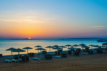 Wall Mural - sunrise, sunset on the beach with umbrellas orange and blue color at dusk.