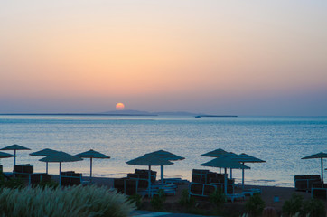 Wall Mural - sunrise, sunset on the beach with umbrellas orange and blue color at dusk.