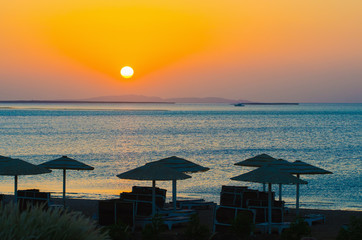 Wall Mural - sunrise, sunset on the beach with umbrellas orange and blue color at dusk.