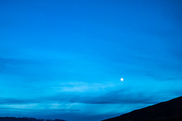 bright moonlight over a blue dusk sky and mountain silhouette