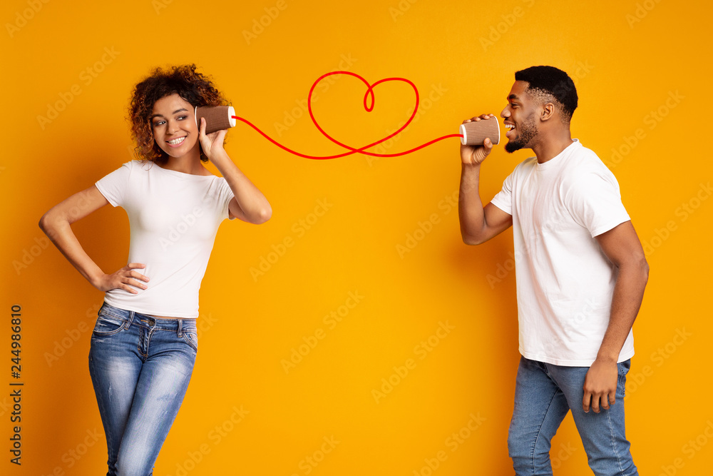 Young black couple with can phone on orange background - obrazy, fototapety, plakaty 