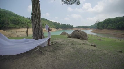 Woman in white bird costume standing next to a tree in front of a big lake.