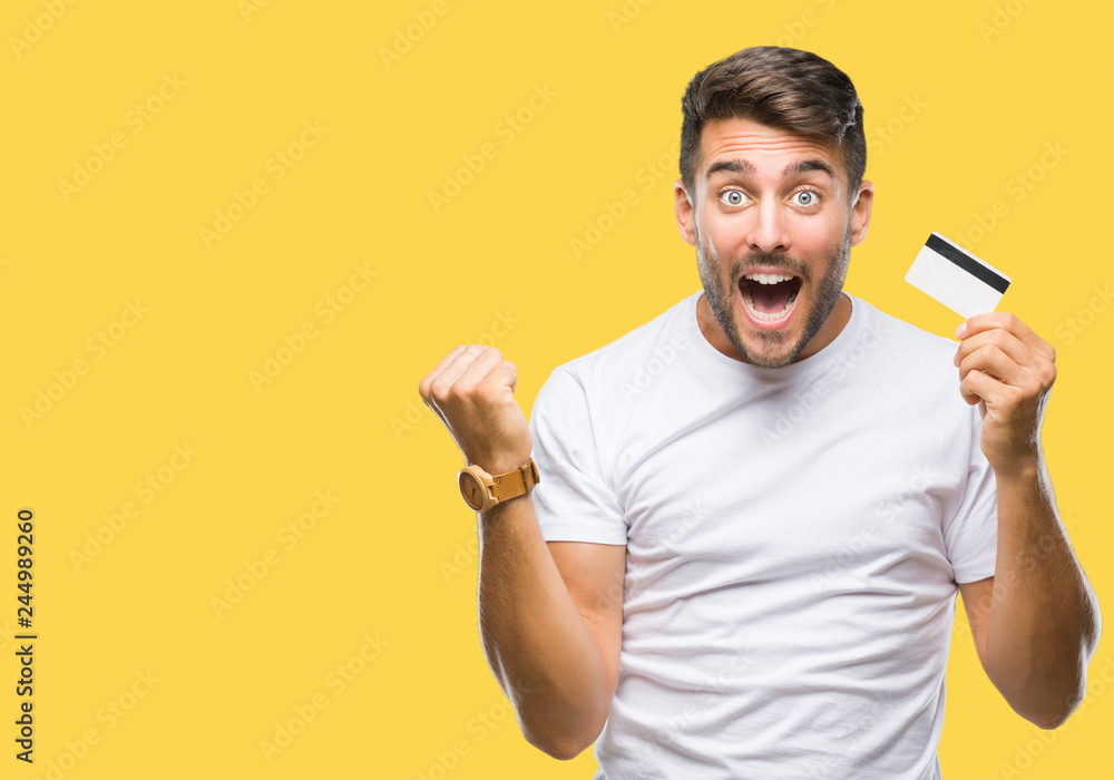 Young handsome man holding credit card over isolated background screaming proud and celebrating victory and success very excited, cheering emotion - obrazy, fototapety, plakaty 
