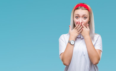 Poster - Young blonde woman wearing headphones listening to music over isolated background shocked covering mouth with hands for mistake. Secret concept.