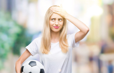 Wall Mural - Young beautiful blonde woman holding soccer ball over isolated background stressed with hand on head, shocked with shame and surprise face, angry and frustrated. Fear and upset for mistake.