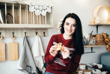 A cute girl sits on a table in the kitchen and eats cookies with chocolate crumbs