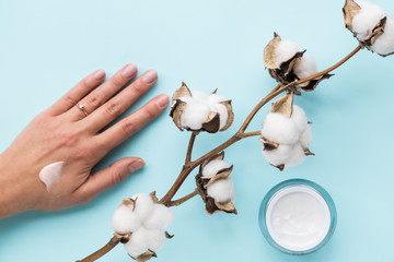 Poster - Cotton flower on pastel pale blue paper background, cream and female hand, overhead. Minimalism flat lay composition for bloggers, artists, social media, magazines. Copyspace, horizontal