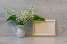 Bouquet Of Fresh Lily Of The Valley Flowers And Empty Photoframe On Light Wooden Background. Beautiful Spring Still Life, Mock Up For Greeting Card, Good Morning Concept