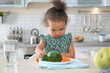 Cute African-American girl with plate of vegetables at table in kitchen