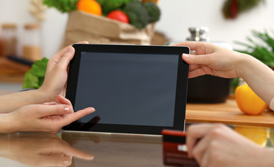 Close-up of human hands using tablet or touch pad. Two women in kitchen. Cooking, friendship or online shopping concepts