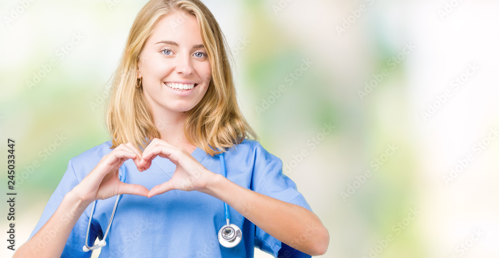 Beautiful young doctor woman wearing medical uniform over isolated background smiling in love showing heart symbol and shape with hands. Romantic concept.