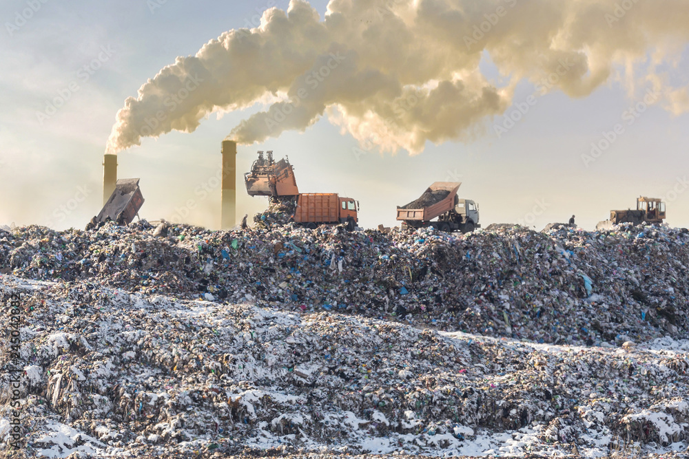 Dump trucks unloading garbage over vast landfill. Smoking industrial stacks on background. Environmental pollution. Outdated method of waste disposal. Survival of times past - obrazy, fototapety, plakaty 