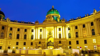 Wall Mural - Vienna, Austria. Illuminated Hofburg Palace seen from Michaelerplatz at night. Motion blurred people, clear bluesky. Popular landmark in the city. Night time-lapse, zoom in