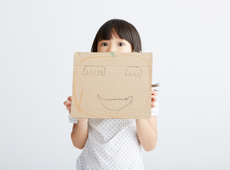 Asian little girl playing with paper mask, in white background