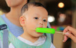© zilvergolf - Adorable Asian baby boy sucking ice-cream by people hand.