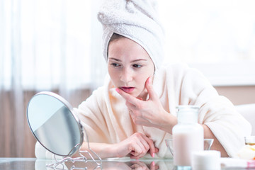 Beautiful happy woman with a towel on her head looking at her skin in a mirror. Concept of hygiene and care for the skin