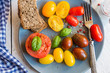 Red, yellow and brown tomatoes on a plate with herbs, spices and bread