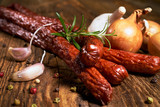 Fototapeta  - Smoked sausage on a wooden rustic table with the addition of fresh aromatic herbs and spices, natural product, produced by traditional methods