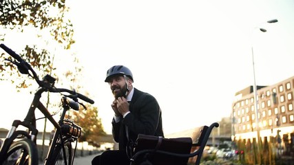 Wall Mural - Businessman commuter traveling home from work in city, sitting down on a bench.