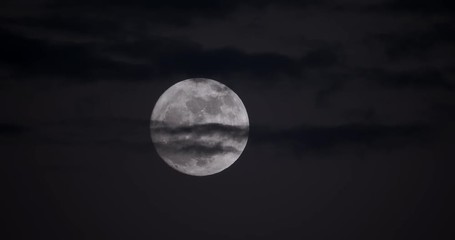 Wall Mural - Spectacular shot of a full moon hiding behind cool looking clouds at dusk in 4K.