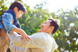 asian father lifting child son in joy outdoors in a park