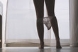 © flowertiare - Bottom view of silhouette of beautiful woman with sexy legs taking off her white panties in a room against the backdrop of curtains