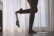 © flowertiare - Bottom view of silhouette of beautiful woman with sexy legs taking off her white panties in a room against the backdrop of curtains