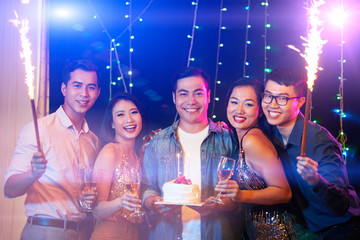 Happy handsome Vietnamese man with birthday cake gathered his friends in night club