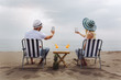 © Mediteraneo - Couple on a deck chair relaxing on the beach using phone. Happy couple enjoy on the beach during summer vacations