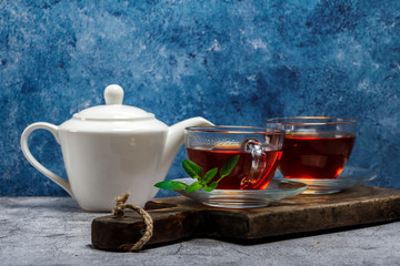 Wall Mural - Tea in a glass cup on a wooden board with a blue and gray background. Close-up. Cup of tea with teapot on a blue gray background.