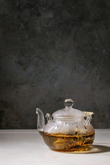 Hot green tea in transparent glass teapot standing on white marble table.