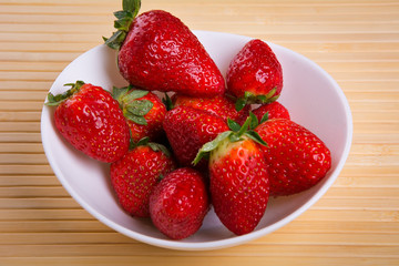 Strawberry in white plate close-up on light background