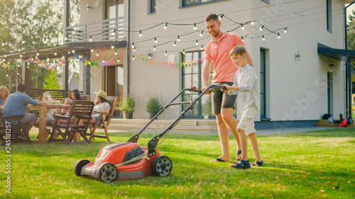Fotomural  Good Father Teaches Son How to Use Walk Behind Lawn Mower, They Push it Together, Cutting Grass