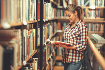 Wall Mural - Young female student read and learns by the book shelf at the library.Reading a book.