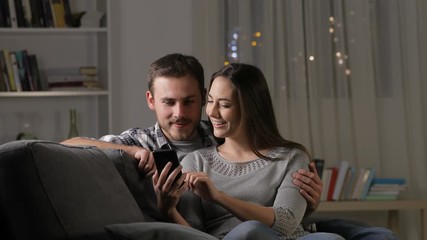 Sticker - Excited couple finding amazing smart phone content sitting on a couch in the living room at home